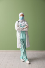 Sticker - Female Muslim doctor in hijab and face mask on green background. World Hijab Day concept