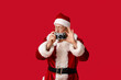© Pixel-Shot - Santa Claus in glasses with camera taking photo on red background