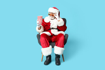 Sticker - Santa Claus in 3D glasses with bucket of tasty popcorn on blue background