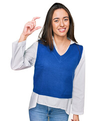 Poster - Young hispanic girl wearing casual clothes smiling and confident gesturing with hand doing small size sign with fingers looking and the camera. measure concept.