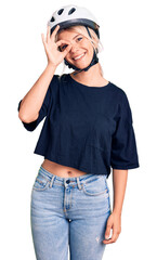 Poster - Young beautiful blonde woman wearing bike helmet smiling happy doing ok sign with hand on eye looking through fingers