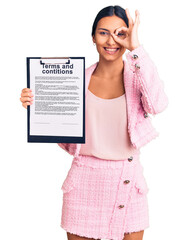 Poster - Young beautiful latin girl holding clipboard with terms and conditions document smiling happy doing ok sign with hand on eye looking through fingers