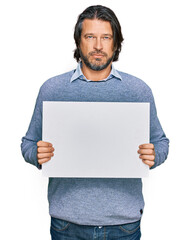 Canvas Print - Middle age handsome man holding blank empty banner thinking attitude and sober expression looking self confident