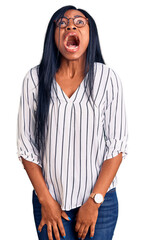 Poster - Young african american woman wearing casual clothes and glasses angry and mad screaming frustrated and furious, shouting with anger. rage and aggressive concept.