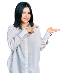 Poster - Young brunette woman with blue eyes wearing oversize white shirt amazed and smiling to the camera while presenting with hand and pointing with finger.