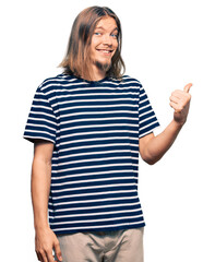 Wall Mural - Handsome caucasian man with long hair wearing casual striped t-shirt smiling with happy face looking and pointing to the side with thumb up.