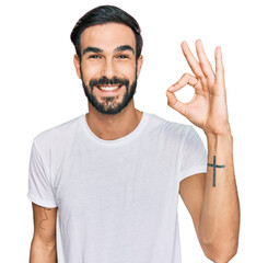 Wall Mural - Young hispanic man wearing casual white t shirt smiling positive doing ok sign with hand and fingers. successful expression.