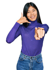 Poster - Beautiful young asian woman wearing casual clothes smiling doing talking on the telephone gesture and pointing to you. call me.