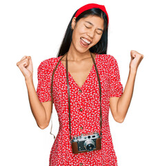 Sticker - Beautiful young asian woman wearing dress and vintage camera very happy and excited doing winner gesture with arms raised, smiling and screaming for success. celebration concept.