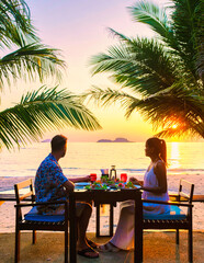 Wall Mural - couple having a romantic dinner on the beach of Koh Chang Thailand during sunset, men and woman dinner on the beach at sunset with palm trees at a luxury resort during vacation honeymoon