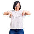 © Krakenimages.com - Brunette woman with down syndrome wearing casual white tshirt pointing down with fingers showing advertisement, surprised face and open mouth