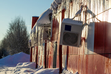 Street block conditioner frozen and covered with icicles and snow in winter. Air conditioner hanging on hoses