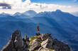 Adventurous athletic male hiker standing on top of a rugged mountain in the Pacific Northwest with jagged mountains in the background.
