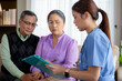 © NT_studio - Caregiver sitting on sofa checkup and diagnostic with elderly couple patient about health in living room at home, caretaker sitting on couch explaining and examining senior, insurance and medical.
