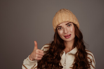 A beautiful European-looking girl in a beige large-knit hat and sweater on a gray background