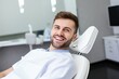 © Stavros - Close-up photo of a young smiling man sitting in a chair in a dental office. He is waiting for the dentist for an oral procedure. Teeth whitening concept.