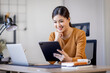 © David - Young modern business asian woman working using digital tablet while sitting in the home office