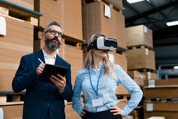 Canvas Print - Warehouse managers talking logistics using VR, controlling stock levels. Virtual reality in inventory management. Smart glasses guiding female manager through warehouse, recording tracking data and