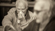 An elderly man with a cold blows his nose at home