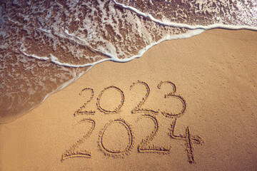Wall Mural - Starting new year 2024 ending 2023 text on the beach sand and splashing sea wave seasonal background