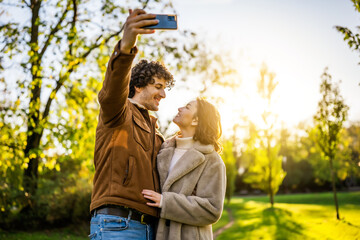 Wall Mural - Portrait of happy loving couple in park in sunset. They are taking selfie.