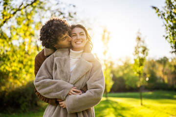 Wall Mural - Happy loving couple embracing and kissing in park in sunset.