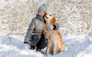 Wall Mural - Teenage Girl And Golden Retriever Sit Together In Snow-Covered Forest During Winter