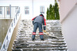 Utility worker shoveling snow and ice from stair case on city street. Man shoveling snow and icy stairs steps. Street cleaner cleaning the staircase overpass blizzard