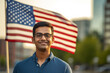 Portrait of a young Indian man with glasses studying, with USA flag in the background. Happy exchange student in blue t-shirt in front.generative ai