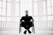 © GVS - Handsome young man sits in chair against background of large bright windows.