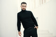 © GVS - Handsome fashionable man model in an all-black clothing outfit posing on white staircase