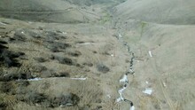 Aerial View Of The Valley Of A Winding Small Mountain River. Snow Thawed Along The Banks, Trees Without Leaves. Deserted Gray Mountains In Winter Without Grass. Drone Footage. Direct Flight. Armenia