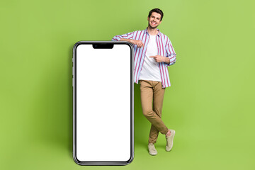 Poster - Full length body photo of young handsome businessman promoter marketing directing finger phone display isolated on green color background