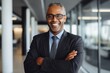 © Carlos - African American Black businessman arms crossed smiling looking at camera in modern office wearing eyeglasses