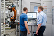 © Westend61 - Businessman and employee standing at control panel in a factory