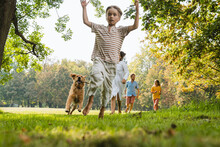 Playful Boy Running With Dog And Family On Grass At Park