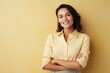 © Carlos - Stylish brunette entrepreneur businesswoman with arms crossed, smiling, looking at camera, against a yellow background.