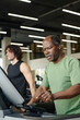 © AnnaStills - Black man about to press key on treadmill at gym with caucasian man training on background
