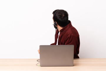 Wall Mural - Telemarketer caucasian man working with a headset and with laptop in back position and looking side.