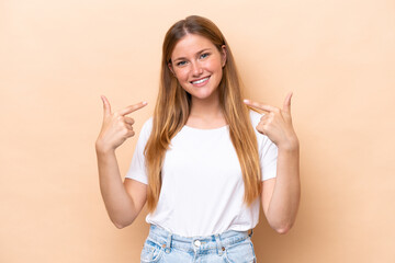 Wall Mural - Young caucasian woman isolated on beige background giving a thumbs up gesture