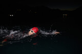 Fototapeta Nowy Jork - A determined professional triathlete undergoes rigorous night time training in cold waters, showcasing dedication and resilience in preparation for an upcoming triathlon swim competition