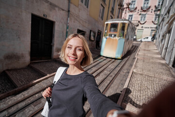 Wall Mural - Traveling by Portugal. Happy young woman with rucksack taking selfie in Lisbon.