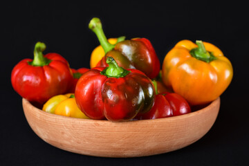 Wall Mural - bright red and yellow bell peppers in a wooden bowl, close-up, dark background, no people