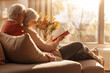© Peeradontax - Concept of love language. Back side view, Close up at elder couple's hand embrace around shoulder and read a book on the sofa. Love on cozy sunny warm vibe living room background