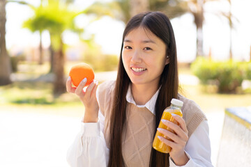 Wall Mural - Pretty Chinese woman at outdoors holding an orange and an orange juice