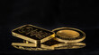 Gold bars and 2 troy ounce gold coin on a black mirror background. Selective focus.