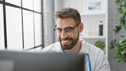 Confident young hispanic man working as a doctor at the clinic, smiling behind the computer