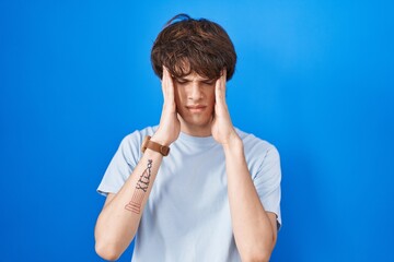 Poster - Hispanic young man standing over blue background with hand on head, headache because stress. suffering migraine.