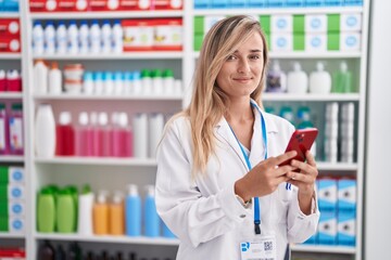 Sticker - Young blonde woman pharmacist using smartphone working at pharmacy