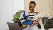 © Krakenimages.com - Beautiful african american woman unpacking a gift at home while relaxing on her sofa and engaging in a cozy video call